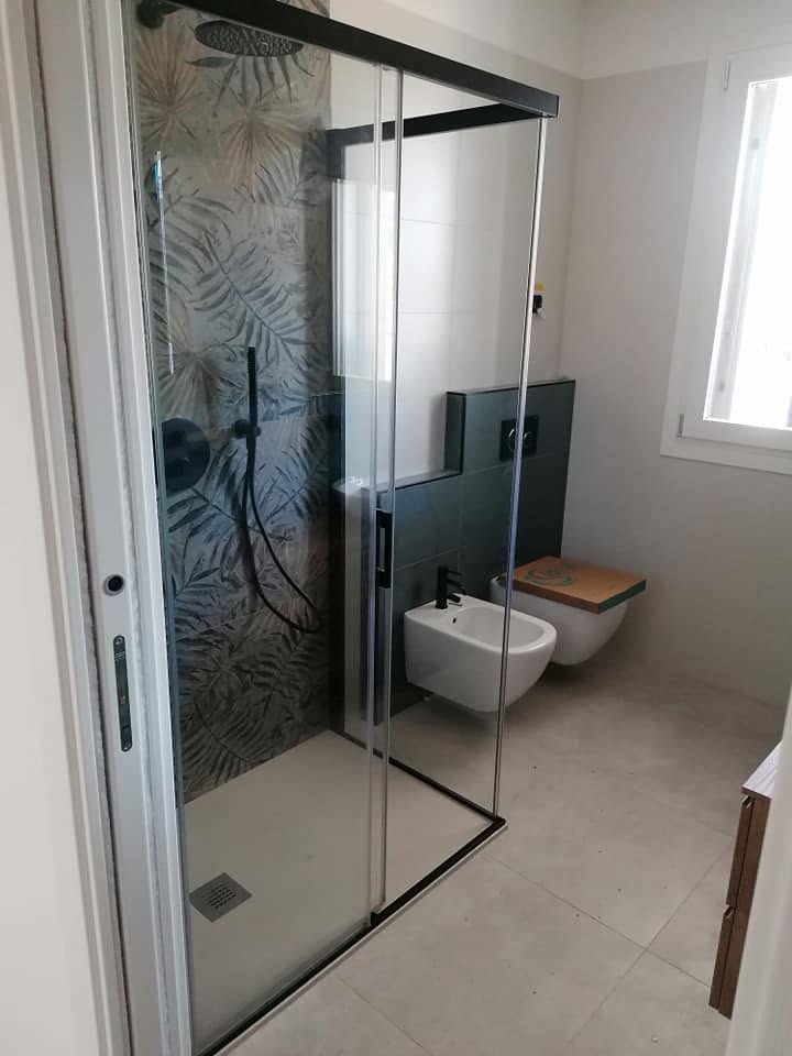 Bagno realizzato con doccia in vetro e rivestimento decorativo botanico